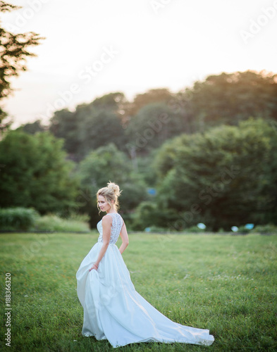 Bride in elegant dress walks across the green lawn in a bright day © IVASHstudio
