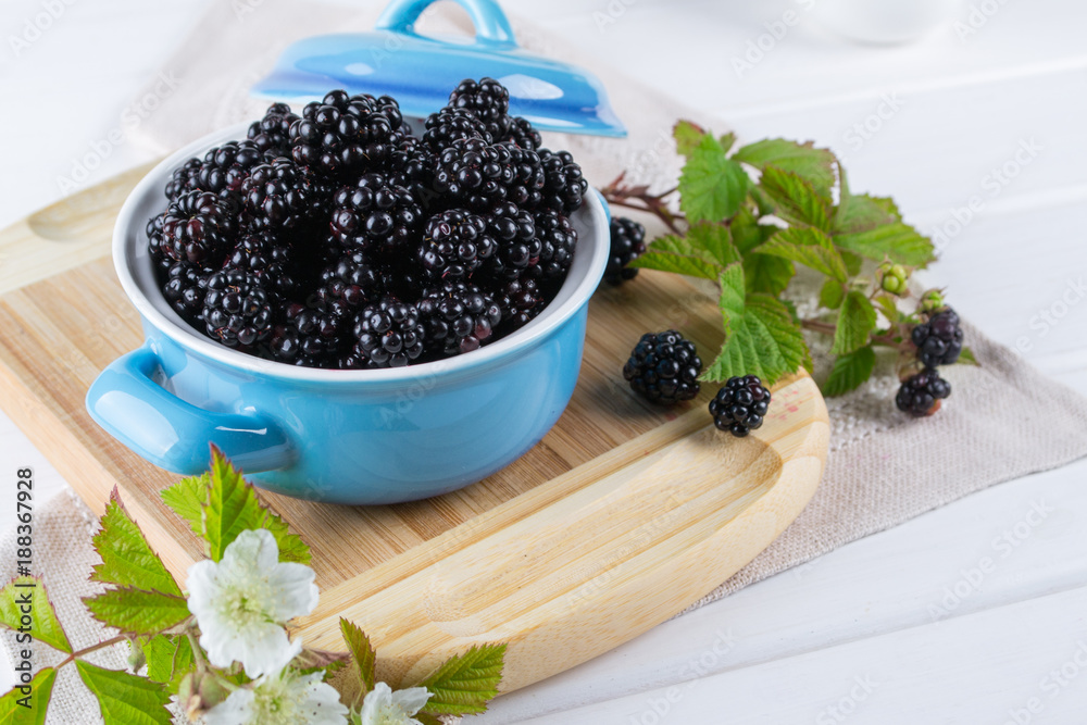Ripe blackberries with leaves in a blue ceramic bowl on white table Ripe blackberries with leaves in a blue ceramic bowl on white table