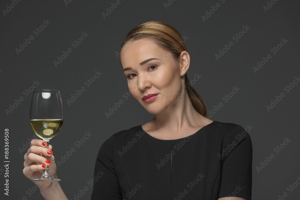 smiling kazakh woman holding glass of wine and looking at camera isolated on grey smiling kazakh woman holding glass of wine and looking at camera isolated on grey