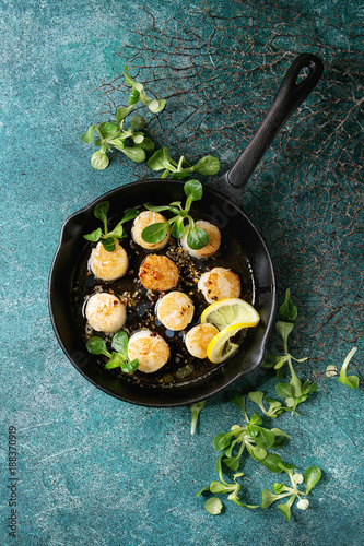 Fried scallops with butter lemon spicy sauce in cast-iron pan served with green salad over turquoise texture background. Top view, copy space