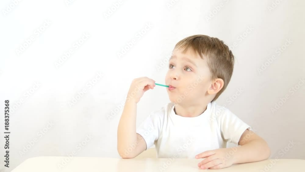 Baby boy smiling and eating lollipops on a stick, sitting at a table on a white background. Baby boy smiling and eating lollipops on a stick, sitting at a table on a white background.