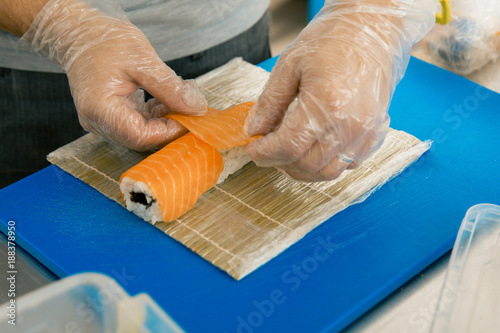 Professional sushi chef preparing roll at commercial kitchen. Cook puts the salmon on roll. Japanese cuisine recipes photo