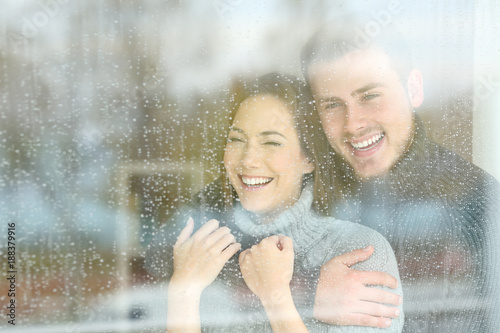 Joyful couple looking through a window a rainy day