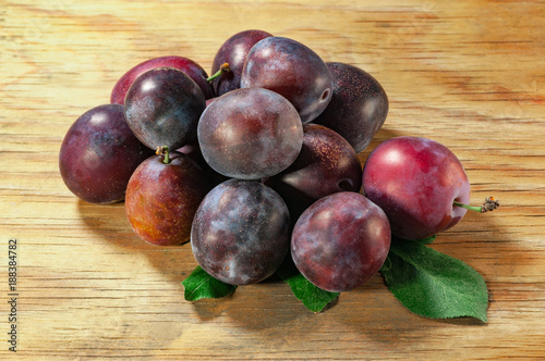 fresh plums with leaves on wooden background