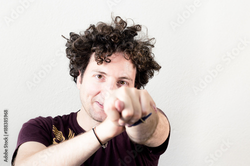 Portrait of a young, Caucasian, brunet, curly haired man showing fig gesture on white background.