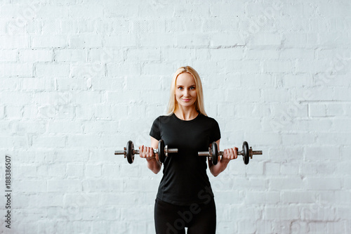 Wallpaper Mural Attractive young fitness woman blonde in red black top against the background of a white brick wall. Studio shot. girl holds folding dumbbells in hand. Torontodigital.ca