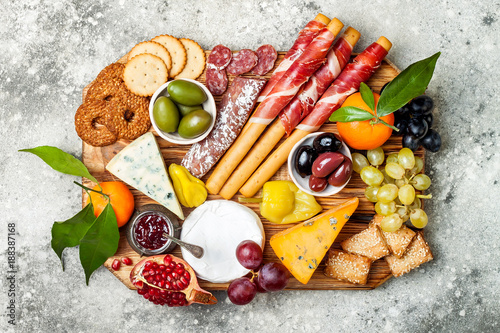Appetizers table with antipasti snacks. Cheese and meat variety board over grey concrete background. Top view, flat lay