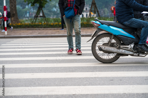 People walking across a street while motorbikes keep running on street in Hanoi, Vietnam. Closeup
