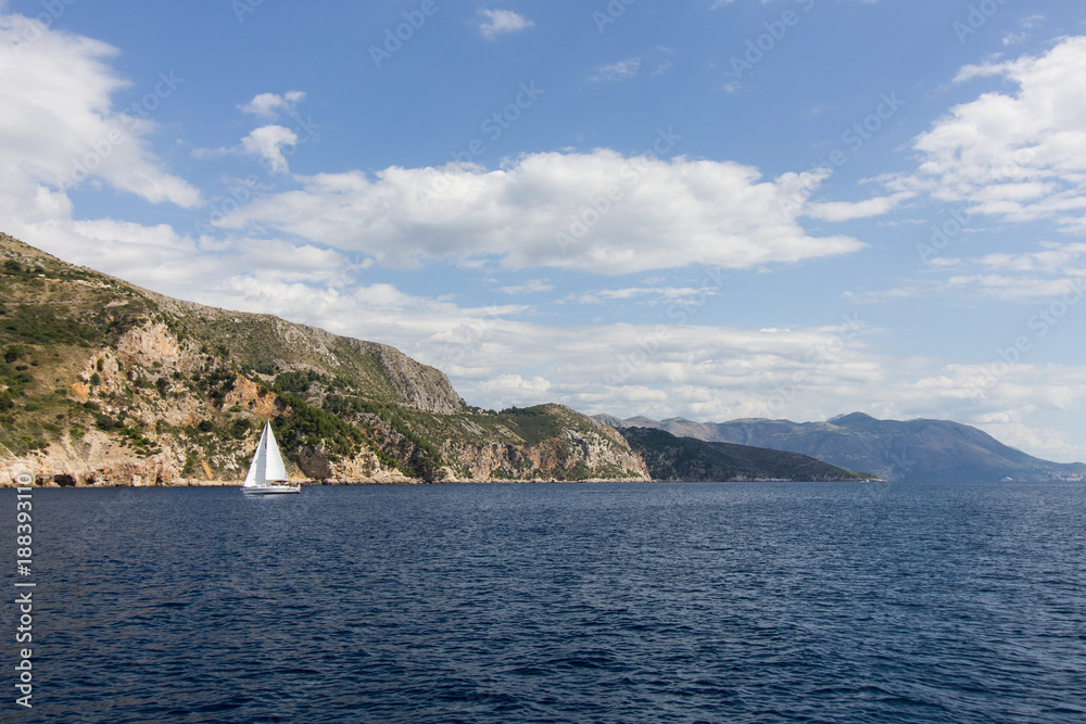 View of a sailing boat at the Adriatic Sea and mountainous coastline near Dubrovnik in Croatia on a sunny day. Copy space. View of a sailing boat at the Adriatic Sea and mountainous coastline near Dubrovnik in Croatia on a sunny day. Copy space.