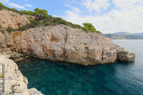 Scenic view of an empty sea cave, shallow water and steep and rugged cliff on the Lokrum Island in Croatia.