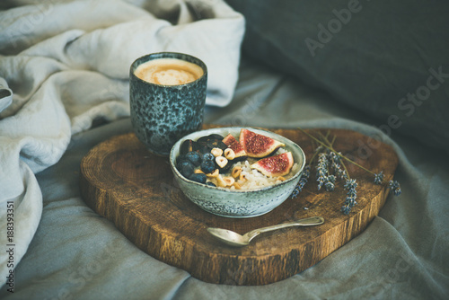 Healthy winter breakfast in bed. Rice coconut porridge with figs, berries and hazelnuts and cup of coffee over rustic wooden board background. Clean eating, alkiline diet, vegan food concept