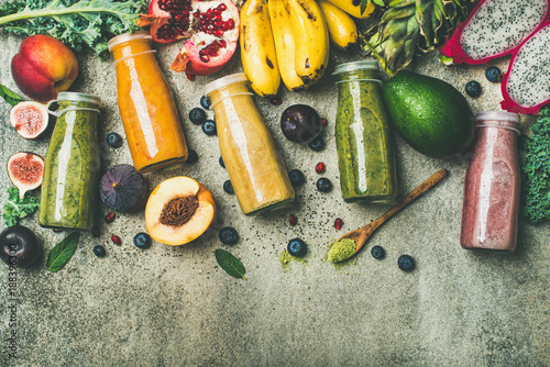 Flat-lay of colorful smoothies in bottles with fresh tropical fruit and superfoods on concrete background, top view, copy space. Healthy, vegetarian, detox, dieting breakfast food concept
