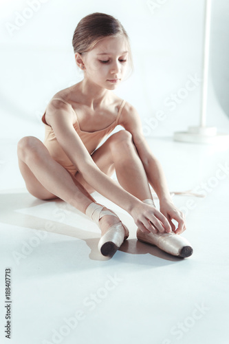 Beautiful little ballerina puting on foot pointe shoes