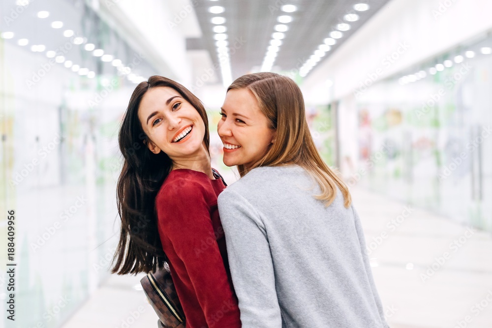 Obraz premium Two happy young girlfriends laugh and talk walking to the shops
