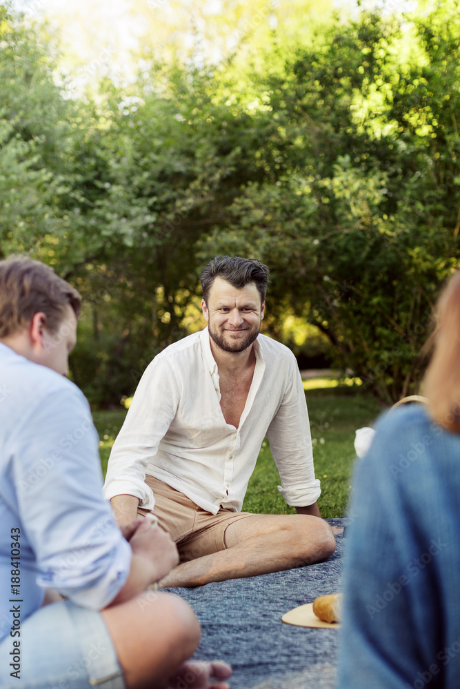 Smiling bearded man sitting with friends at picnic Smiling bearded man sitting with friends at picnic