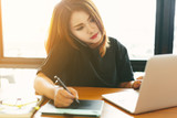 Asian stylish woman designer wear black dress and red lips using smartphone while working with her laptop in selective focus..