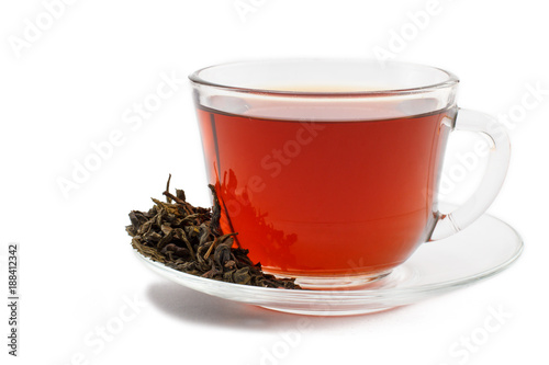 Glass cup of tea on saucer with dry leaves of green tea on white isolated background