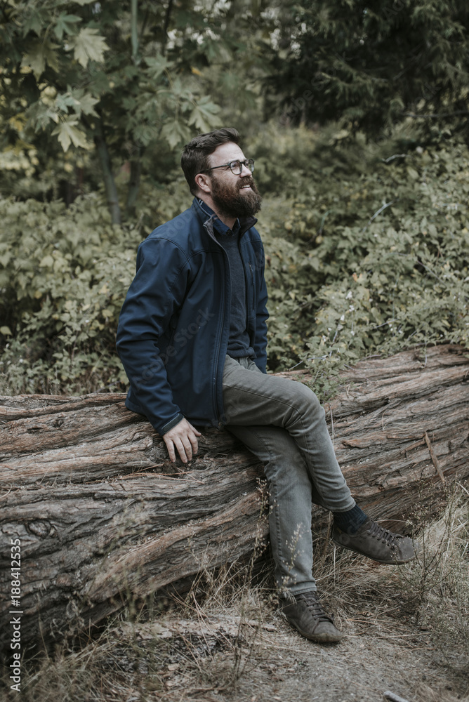 Man looking away while sitting on log in forest at Yosemite National Park