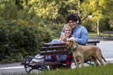 Young couple sitting on the bench with dog beside and listening music over headphones and smile