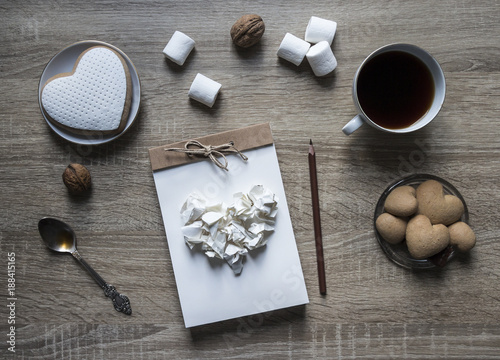 on a wooden background lies a craft notepad scrapbooking plate cookie heart pencil brown mug coffee marshmallow nuts lump paper mint spoon 