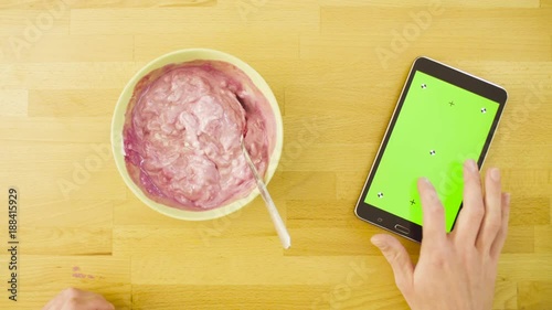 Top view. A tablet with green screen laying on the kitchen table. Man scrolling the tablet and eating cottage cheese