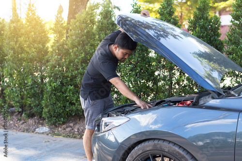 ypung man waits for assistance near his car broken down on the road side, looks under the hood of his car