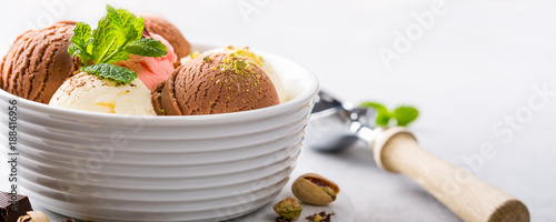 Set of ice cream scoops of different colors and flavours in white bowl with pistachio nuts and mint decoration. Summer food concept with copy space. Banner.