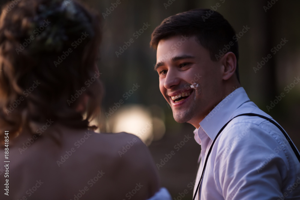 Newlyweds have fun having a wedding cake with candles in the evening in the nature