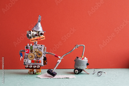 Robot vacuum cleaner machine service. Funny robotic toy metal funnel hopper, cogs wheels gears metallic body, cleaning carpet process, red wall room interior. photo