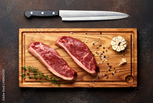 Raw fresh meat Picanha steak, traditional Brazilian cut with rosemary, garlic, knife and black pepper on wooden board. Sliced meat steaks. Top view.