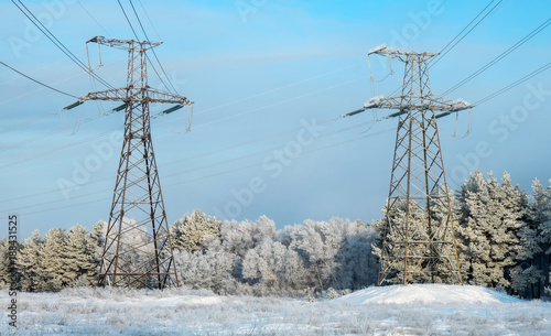 Winter landscape with power lines in a snowy field near the forest and park
