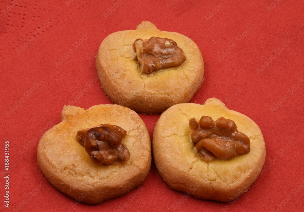Three apple shape cookies or biscuits with one walnut on red background.