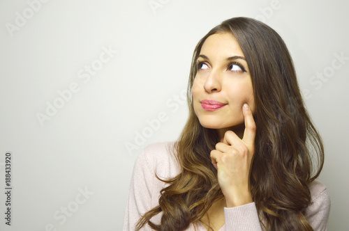 Cute young woman looking to the side the copyspace thinking what to buy on white background