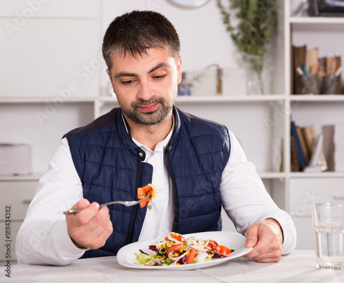Young man looking at vegetable salad and eating