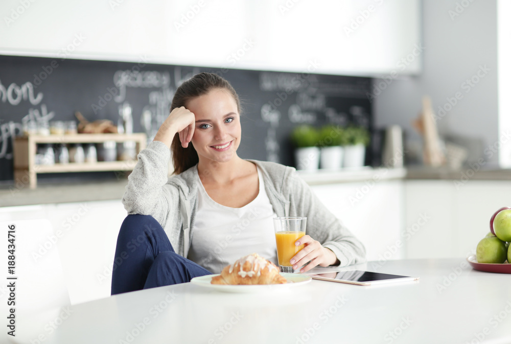 Young woman with orange juice and tablet in kitchen.