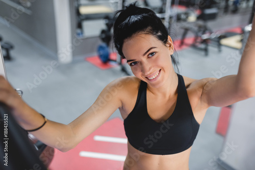 Portrait of beautiful Caucasian smile brunette woman is doing exercises with the bar in the gym, sporty woman exercising with barbell in gym, bodybuilding, people and sport concept.