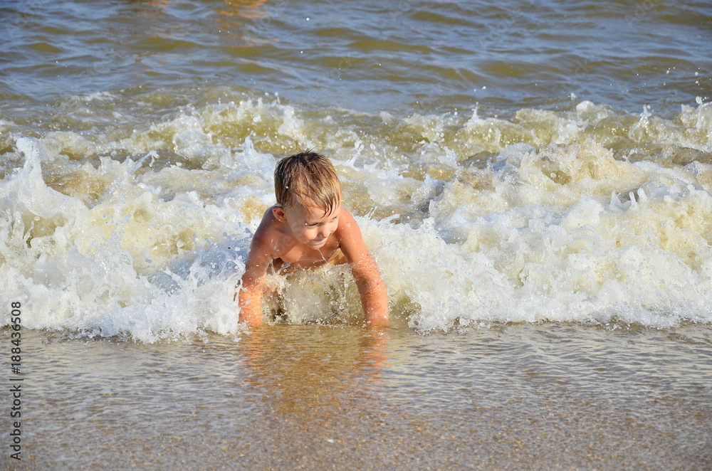 Obraz premium Adorable little blond kid boy having fun on ocean beach. Excited child playing with waves, swimming, splashing and happy about family vacations in Miami, Florida, USA.