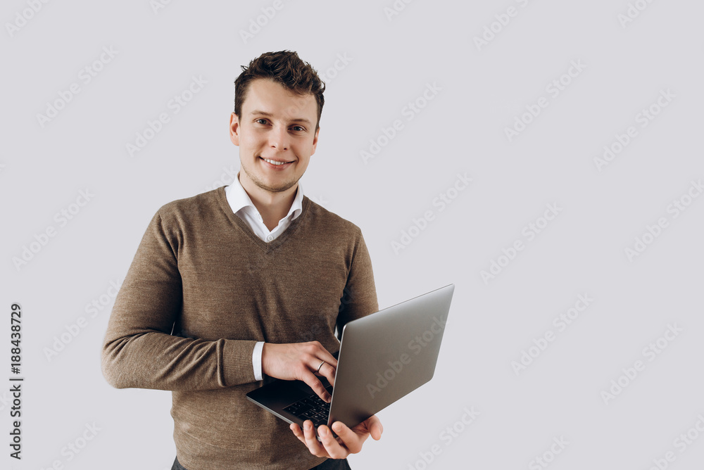 Young smiling guy with laptop in hands stands on white wall background on which there is space for text Young smiling guy with laptop in hands stands on white wall background on which there is space for text
