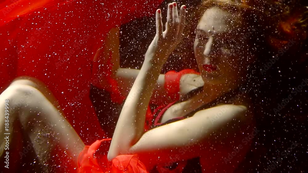 underwater goddess is wearing red dress is swimming in sea water in a deep in dark between tiny bubbles