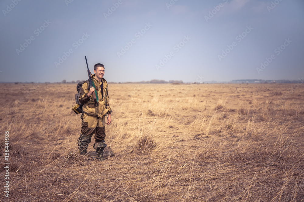 Hunter man with shotgun and hunting equipment standing in dry rural field with dry grass and clear sky during spring hunting season Hunter man with shotgun and hunting equipment standing in dry rural field with dry grass and clear sky during spring hunting season