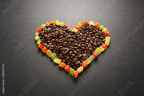Colorful candied fruits in the form of heart with brown coffee beans isolated on black background for design. Saint Valentine's Day card on fabruary 14, holiday concept. Copy space for advertisement.