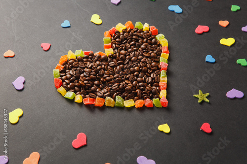 Colorful paper, candied fruits in the form of heart, brown coffee beans isolated on black background for design. Saint Valentine's Day card, fabruary 14, holiday concept. Copy space for advertisement.