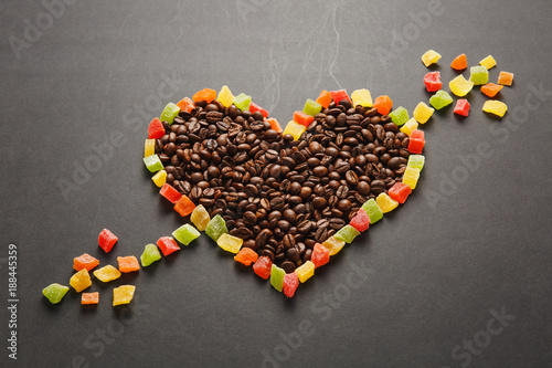 Candied fruits in the form of heart with arrow, brown coffee beans isolated on black background for design. Saint Valentine's Day card on fabruary 14, holiday concept. Copy space for advertisement.