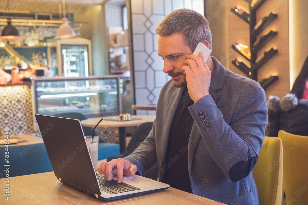 Businessman working in laptop and talking on cellphone in cafe Businessman working in laptop and talking on cellphone in cafe