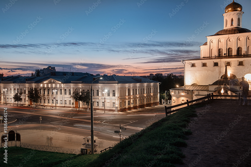 Fototapeta premium night city/ Golden Gate in Vladimir, the earthen rampart and the road. Highlighted buildings at sunset and people silhouettes