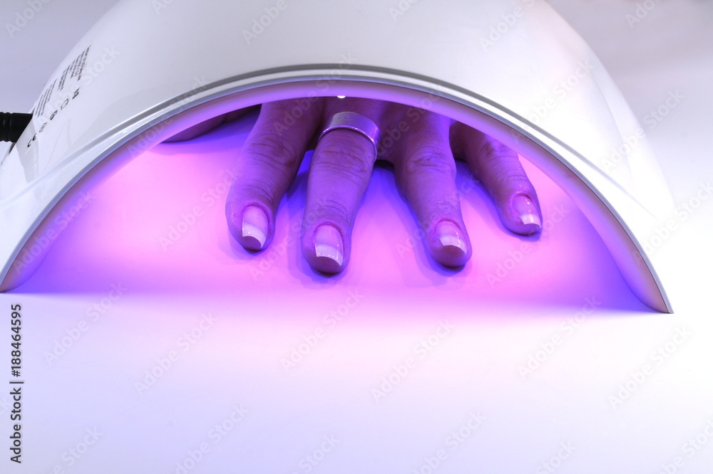 Manicure with uv led lamp, curing gel or hybrid varnish, manicure on table. Hand of a woman under the lamp - obrazy, fototapety, plakaty 