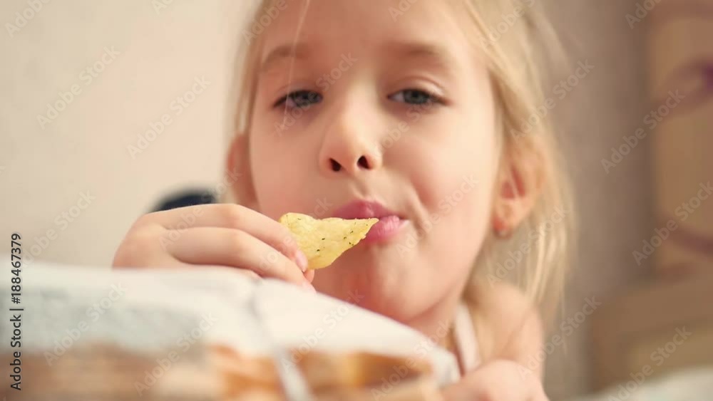 Young girl indoors eating chips smiling. Eating harmful food. Young girl indoors eating chips smiling. Eating harmful food.