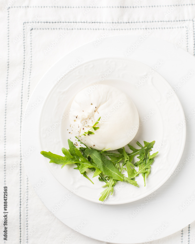Italian cheese Burrata (mozzarella) with fresh arugula, tomatoes, olive oil, sauce pesto on a white plate and a wooden light background. Flat lay, top view Italian cheese Burrata (mozzarella) with fresh arugula, tomatoes, olive oil, sauce pesto on a white plate and a wooden light background. Flat lay, top view