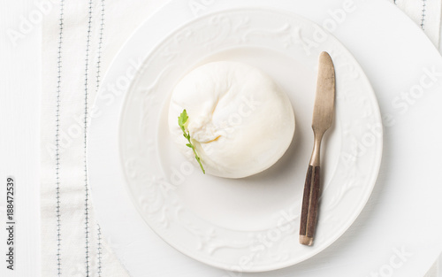 Italian cheese Burrata (mozzarella) with a vintage knife and fresh arugula on a white plate and a wooden light background. Flat lay, top view