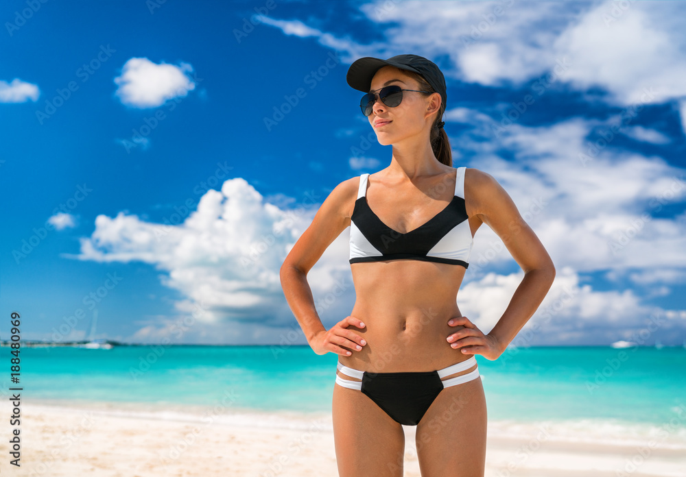 Asian bikini woman on beach summer vacation sporty swimwear girl in sportswear for beach sports. Athlete with fit body wearing solar protection hat and sunglasses, skin care.